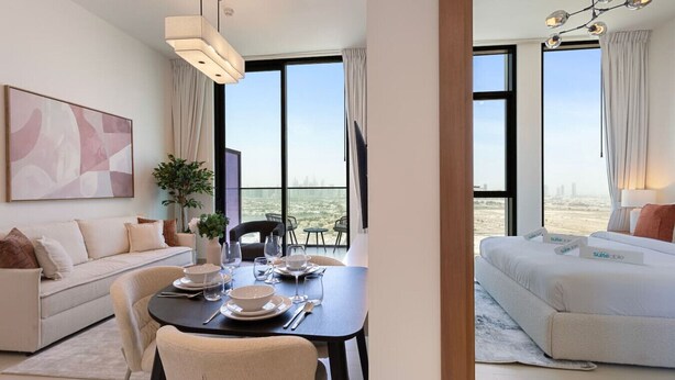 Une chambre d’hôtel moderne dotée d’un coin repas, d’un canapé, d’une grande fenêtre offrant une vue sur la ville et d’un lit donnant sur le paysage urbain.
