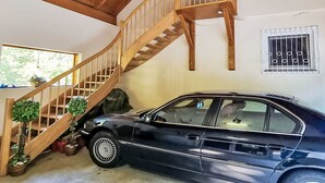 Ein Auto steht in einem Gebäude, eine Holztreppe führt zu einer darüber liegenden Ebene.