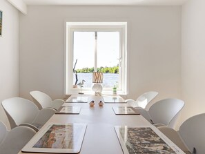 A dining area with a view of a lake, white chairs, a table with placemats, and a lamp. - Vacation home Rönnö by Interhome (Tingsryd)