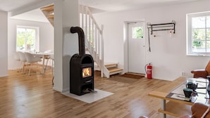 Un intérieur moderne avec un poêle à bois, des murs blancs, un coin repas et un escalier.