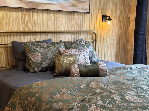Una cama con colcha estampada de flores, cabecera de metal y varias almohadas decorativas.