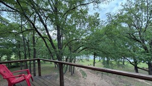 Une terrasse en bois avec des chaises rouges, entourée d’arbres et offrant une vue sur un paysage naturel.