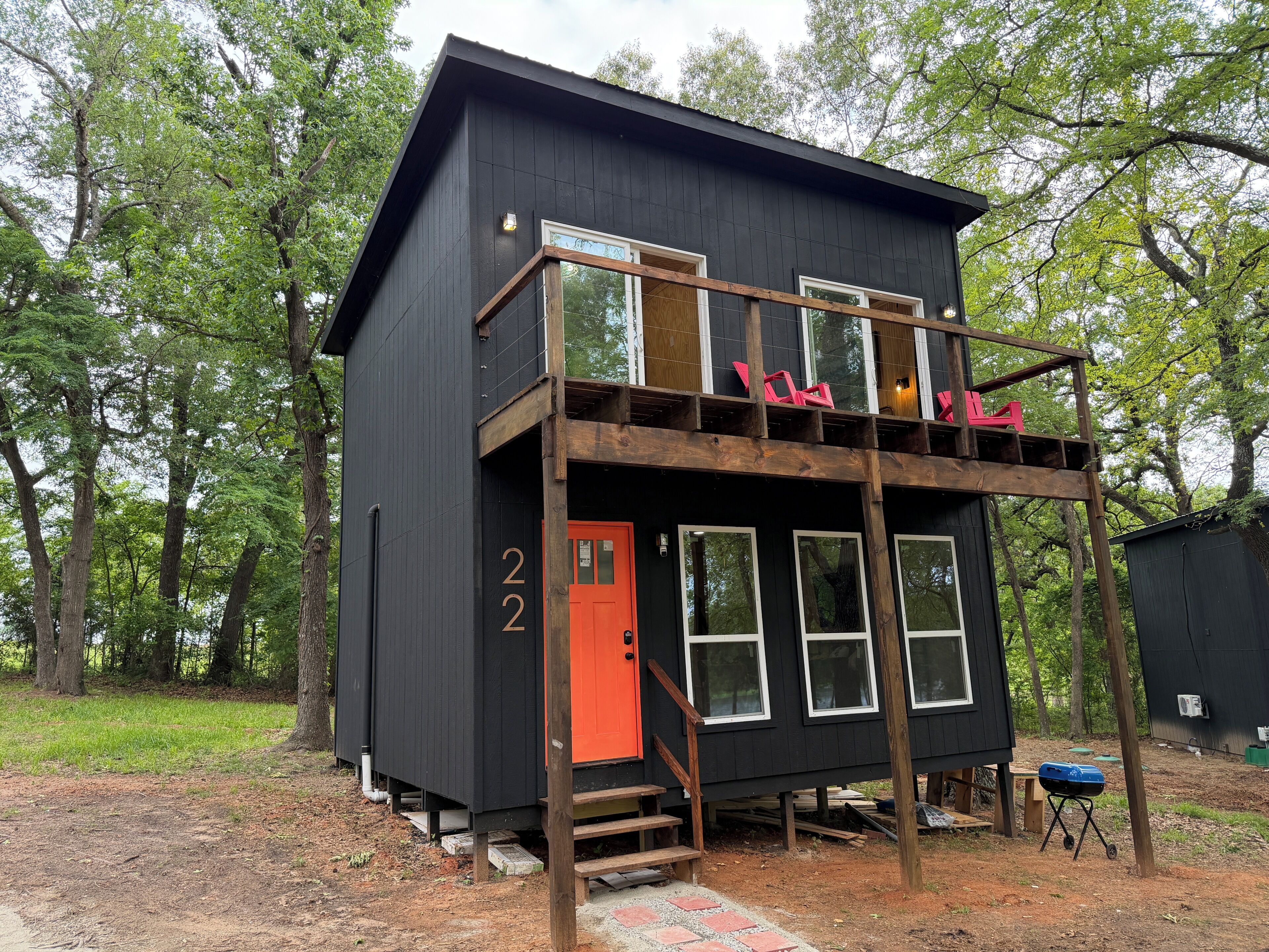 A two-story cabin with a wooden deck, a red door, and a number '22' on the side.