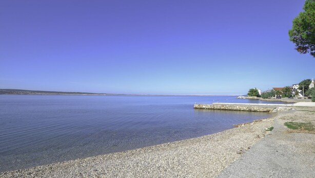 Une plage de galets, avec un ciel bleu clair et une mer calme.
