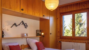 Una habitación con paneles de madera, una cama, un estante con objetos decorativos y un ventanal con vista a árboles.
