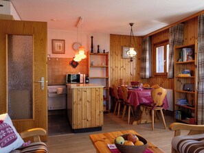 A compact kitchen with a microwave, wooden cabinets, and a dining area with a table set for four. - Edelweiss by Interhome (Veysonnaz)