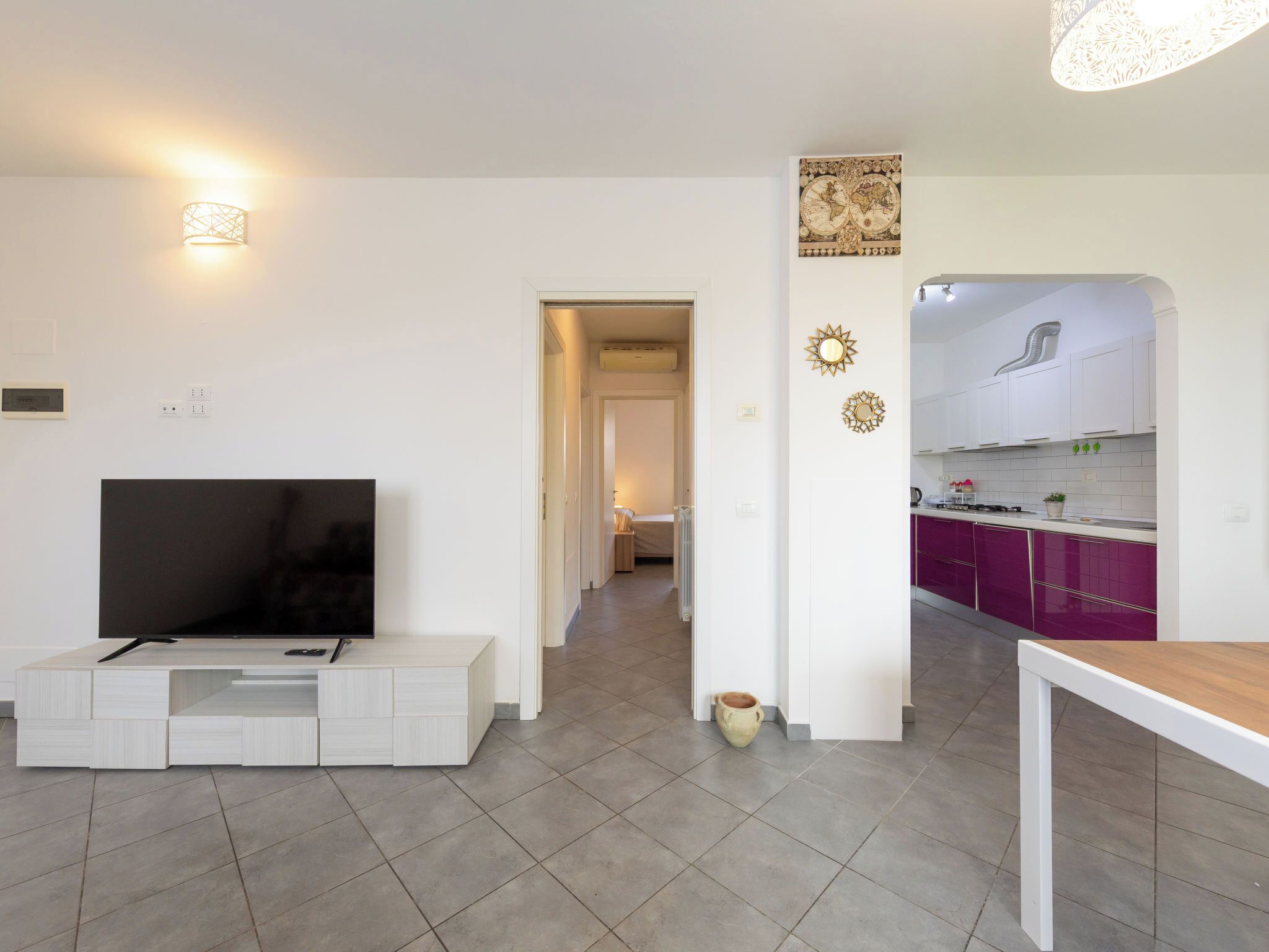 A modern living room with a flat-screen TV, a white entertainment unit, and a dining table.