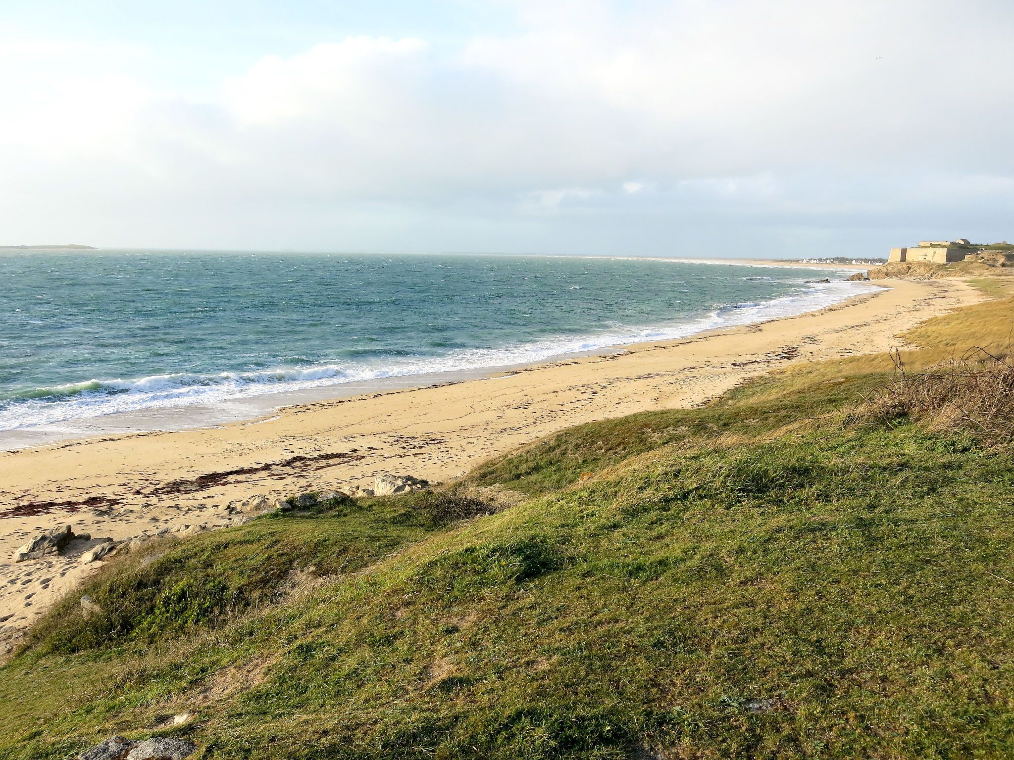 Kustlandschap met een zandstrand, begroeiing en een gebouw in de verte.