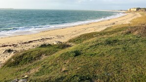 A coastal landscape with a sandy beach, grassy terrain, and a distant building. - Le Chalet du Rohu by Interhome (Quiberon)