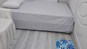 A small, single-bed room with a patterned curtain, a white pillow, and a blue floral rug. - Alaçatı Evi (Cesme)
