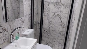 A bathroom with a white sink, toilet, and glass-enclosed shower. - Alaçatı Evi (Cesme)