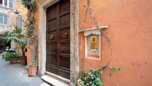 A building with a large wooden door, potted plants, and a small plaque on the wall. - Ninfa Maison Rome | Piazza Navona - Coronari (Roma)