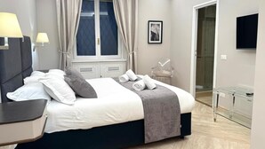 A modern hotel room with a bed, bedside lamps, a window with curtains, a chair, a glass cabinet, and a flat-screen TV. - Ninfa Maison Rome | Piazza Navona - Coronari (Roma)