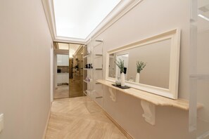 A hallway with a mirror, a shelf with decorative items, and a view into a room with a kitchen. - Ninfa Maison Rome | Piazza Navona - Coronari (Roma)