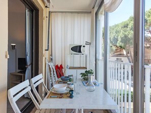 Ein Balkon mit Esstisch für zwei Personen, einer Mikrowelle und einem Blumentopf.