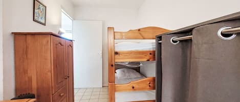 Un dormitorio con una cama litera de madera, un aparador de madera y una puerta que da a otra habitación.