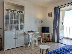 Une chambre avec un lit, une télévision, une petite table avec des chaises, une armoire et un balcon avec des rideaux.