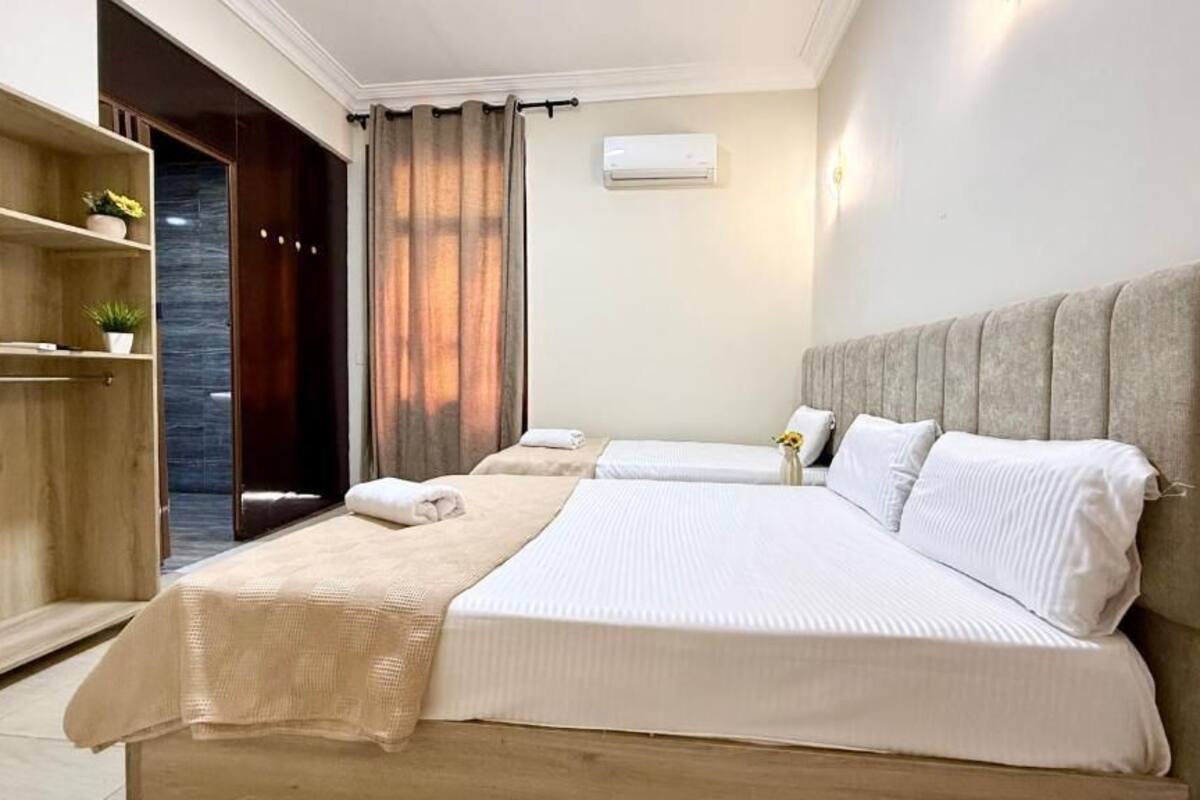 Ein Hotelzimmer mit zwei Betten, einem Holzschrank, einer kleinen Pflanze, einem Vorhang und einer Klimaanlage.