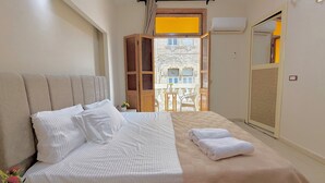 Un dormitorio con una cama grande, un armario de madera, un balcón con vistas a edificios y un equipo de aire acondicionado.