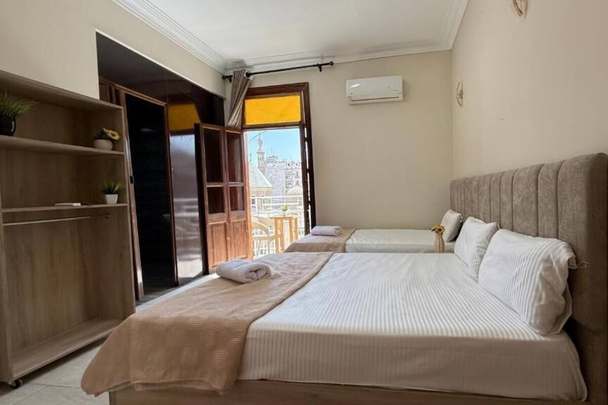 Ein Hotelzimmer mit zwei Betten, einem Kleiderschrank und Blick auf ein Gebäude durch eine offene Tür.