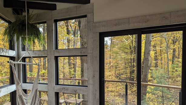 Una habitación con ventanas amplias, una hamaca y vistas a un bosque.