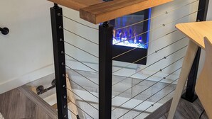 Una escalera de madera con barandilla metálica, una chimenea empotrada en la pared y suelo cubierto de alfombra.