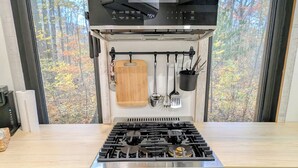 Una cocina con estufa a gas, horno y utensilios colgando.