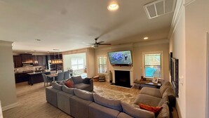 A modern living room with a sectional sofa, a flat-screen TV, a fireplace, and a dining area with a kitchen in the background. - World Cup Ready Spacious 5BR Home Near Atlanta Stadium & Downtown Restaurants (Fairburn)