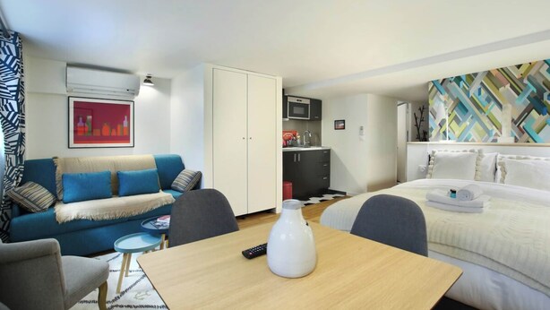 A hotel room with a sofa, a dining table, a bed, a kitchenette, and a TV. - Charming Studio With AC Beaubourg Le Marais (Paris)
