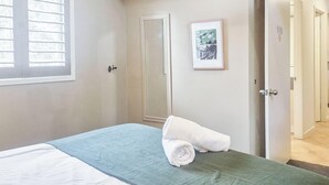 Ein Schlafzimmer mit einem Bett, einem Fenster mit Jalousien, einer Tür und einem gerahmten Bild an der Wand.