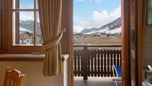 Ein Zimmer mit Fensterblick auf eine verschneite Landschaft, ein Holzstuhl und eine Terrasse mit Zaun.