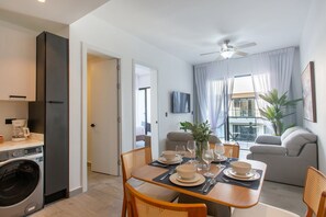 A modern kitchen with a built-in washing machine, a dining area with a table set for four, and a living area with a sofa and a plant. - Pool View, Gym, and Artificial Beach (Punta Cana)
