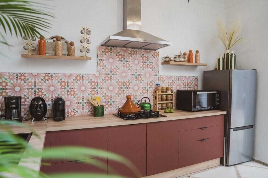 Une cuisine avec un crédence décorée, une cuisinière, un four à micro-ondes, un réfrigérateur et divers ustensiles de cuisine disposés sur le plan de travail.