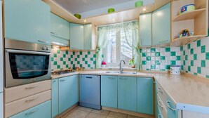Une cuisine avec des armoires de couleur turquoise, un four en acier inoxydable, un lave-vaisselle et une fenêtre avec des rideaux.