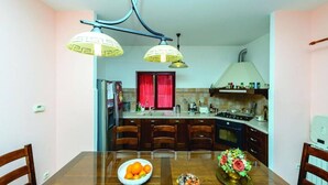 Eine kleine Küche mit Esstisch, Stühlen, einem Kühlschrank, einem Herd und einem Fenster mit roten Vorhängen.
