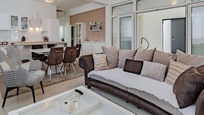 Ein modernes Wohnzimmer mit Sofa, Sesseln, einem Couchtisch und einem Küchenbereich im Hintergrund.