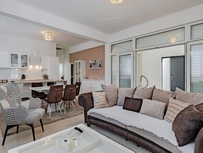 Un salon moderne avec un canapé, des fauteuils, une table basse et un coin cuisine à l’arrière-plan.