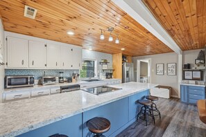 A modern kitchen with wooden ceiling, white cabinets, a large island, and bar stools. - Peaceful Nest: Hot Tub, Fireplace, Fire Pit & MORE (Sevierville)