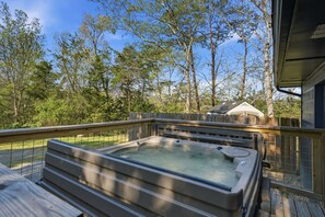 A hot tub on a wooden deck with a view of trees and a house in the background. - Peaceful Nest: Hot Tub, Fireplace, Fire Pit & MORE (Sevierville)