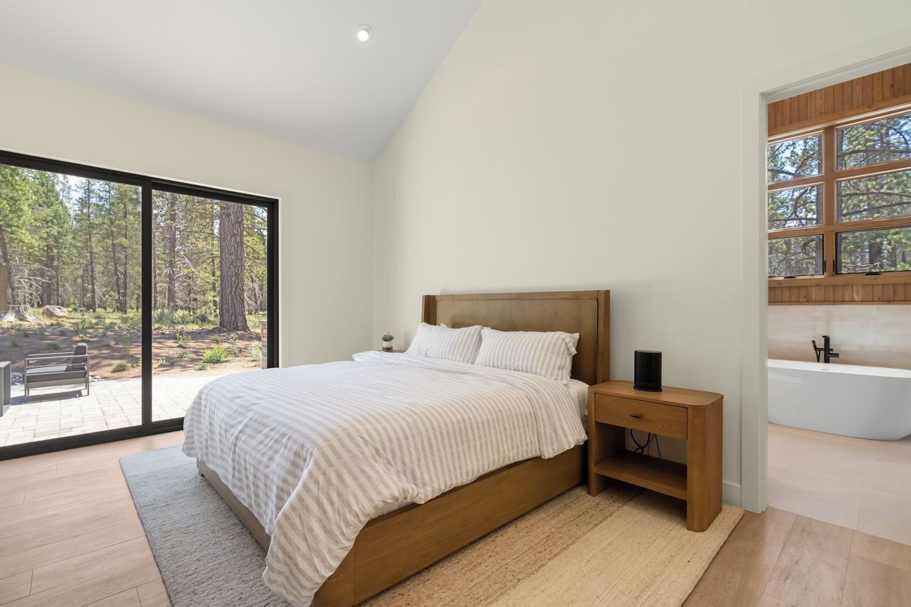 Un dormitorio con una cama grande, una mesita de noche de madera, una bañera empotrada y una puerta de vidrio corredera que da a un área exterior.