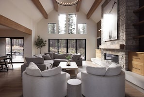 A spacious living room with a stone fireplace, large windows, and a view of the forest.