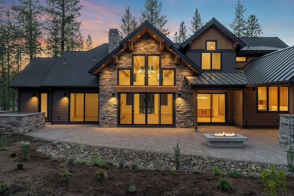 A modern two-story house with a stone facade, large windows, and a fire pit in the front yard.