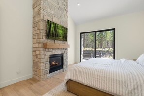 A bedroom with a stone fireplace, a bed, and a large window with a forest view.