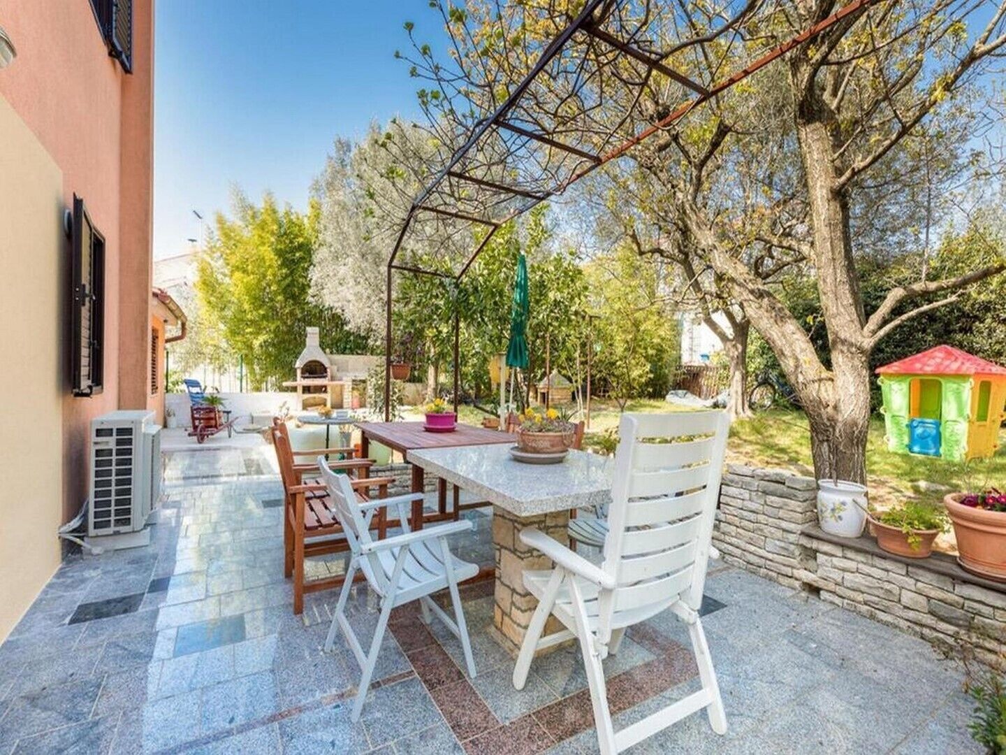 Een terras buiten met een tafel, stoelen, een barbecue en een speelhuisje.