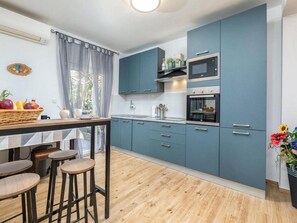 A compact kitchen with blue cabinets, a microwave, and a sink. There are stools at a wooden table and a basket of fruit on the counter. - Family Frendly Holiday Home with Pool (Fažana)