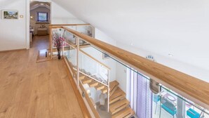 Un interior espacioso con una escalera de madera, barandilla de vidrio y vistas al exterior.