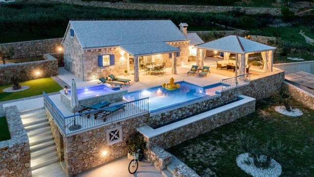 Una casa de piedra con piscina, mobiliario exterior y un patio cubierto.