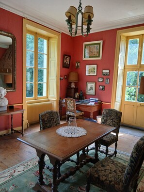 A room with a wooden table, floral armchairs, a chandelier, and a large window with a view of greenery. - Large family home in the heart of nature near the Brière regional park (12p) (Saint-Lyphard)