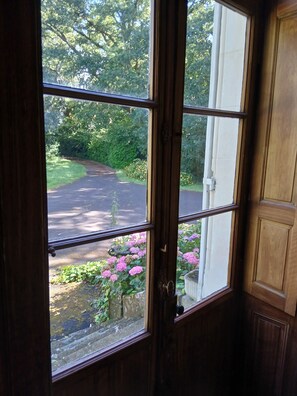 A view through a window with a wooden frame, a door, and a view of a road and greenery outside. - Large family home in the heart of nature near the Brière regional park (12p) (Saint-Lyphard)