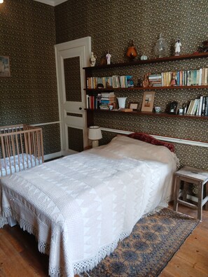 Ein Schlafzimmer mit Bett, Babybett, Bücherregal und einer Tür.